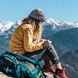 Young woman sitting on mountain and writing in notebook