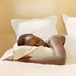 Black woman lying in bed with eyes closed.