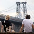 Individuals sitting by a bridge.
