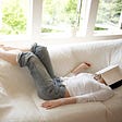 Woman sleeping on sofa in living room, book covering face.