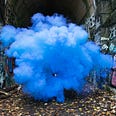 Bright blue smoke at the entrance of a stone walled tunnel covered with grafitti
