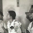 Three Black women singing at church. two have their eyes closed and hands raised in worship