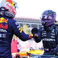 Max Verstappen and Lewis Hamilton shake hands right after a race and still wearing their helmets. Verstappen has his back to camera, Hamilton facing forwards