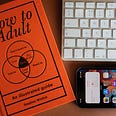 An image of a book titled How to Adult. With a partial keyboard and phone