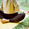 woman sits on yoga mat in grass and meditates