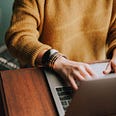 Close up of a person in a yellow sweater typing on a laptop keyboard