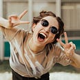 photo of young woman, mouth wide, sunglasses, two V-signs, happy