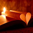 A Bible-looking book is lays open near a candle. two pages are folded into ht center forming a heart shape when seen from the bottom or top. the heart glows golden in the candlelight. but it could be a dictionary!