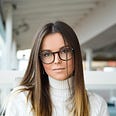 Woman wearing horn-rimmed AI-enabled glasses and white poloneck in office