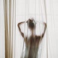 Woman standing behind sheer curtain in front of window.