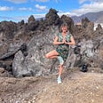 I’m standing on one leg in this picture (I’m a woman in my fifties). There are volcanic rocks behind — this is Tenerife — and cliffs in the distance, and a glimpse of blue sea.