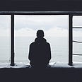 Silhouette of a person alone in a building facing a big window that looks out over a big body of water