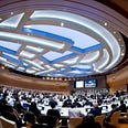 A distorted, fish-eye lens view of a UN conference. Hundreds of delegates sit at desks at a 2016 meeting on Human Rights, Democracy, and the Rule of Law in Geneva, Switzerland.