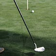 Ball approaches a hole with pin in, putter head and shaft in foreground