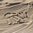 Two handprints in the sand. They face oneanother.