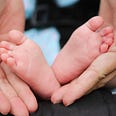 The tiny feet of a small child are gently cradled in loving hands…