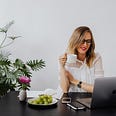 Business woman drings coffee and eats grapes at work over her laptop