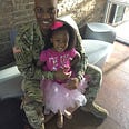 A Soldier posing with his daughter on a bench inside a lobby.