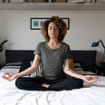 A woman sits on her bed and practices mindfulness through meditation.