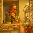 Smiling woman in mirror photographing herself holding a hollow lightbulb