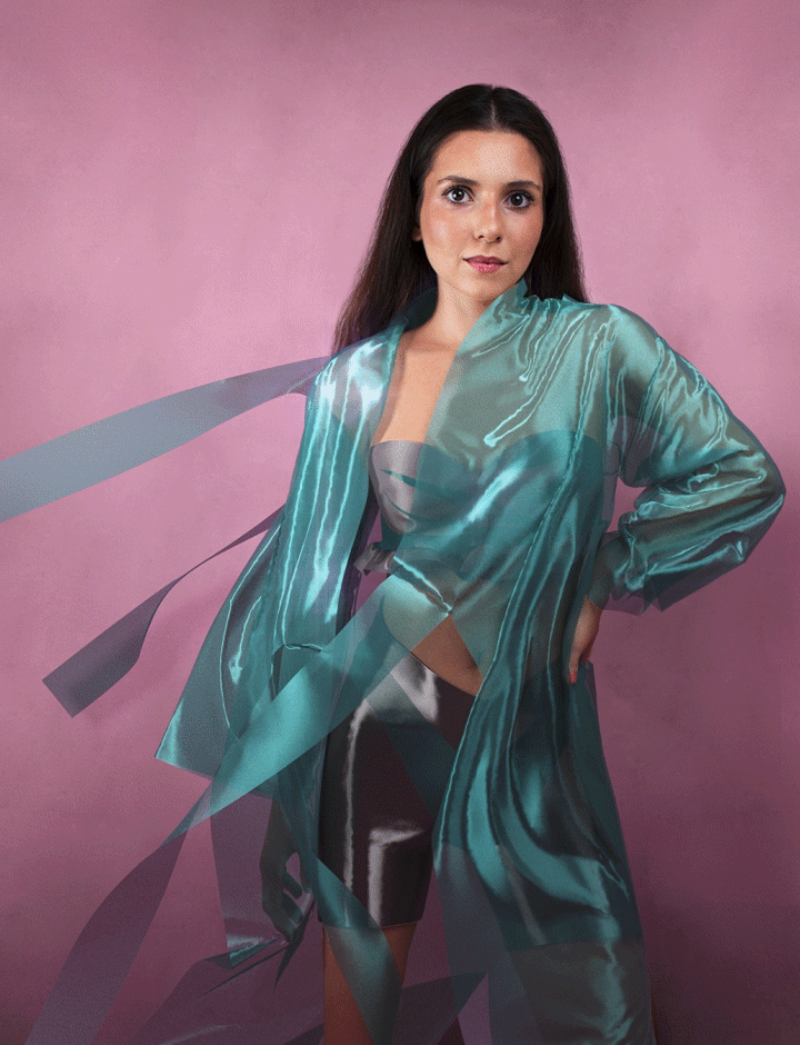 The outcome of a Dress-X purchase, modelled by Eva Sviridova. A glossy, teal dress flowing in an obviously digital breeze.