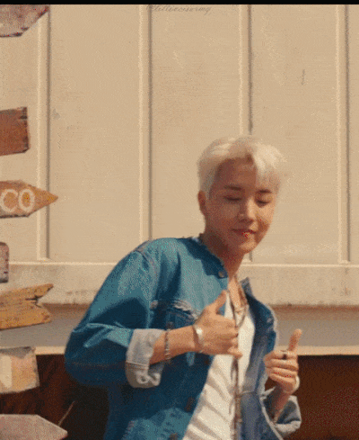 BTS dancing in the music video for Permission to Dance. They are making various signs while dancing. J-Hope is lifting his thumbs up and down at his chest. BTS with Suga in the middle are making sign for “dance” in ASL. RM and V are dancing with hands in the air making peace signs. BTS with Suga in the middle are making sign for “walk”.