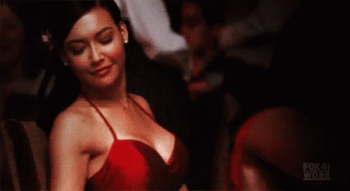 Santana from Glee in a red spaghetti strap dress shaking her shoulders and laughing