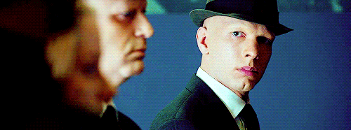 Man in suit and black hat looks distrustfully at several men in front of him.