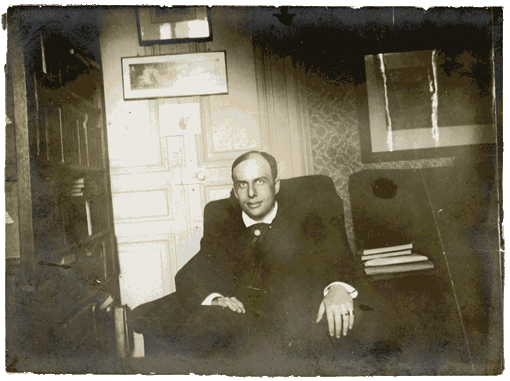 Old photograph of Marcel Schwob sitting in a chair in a living room.