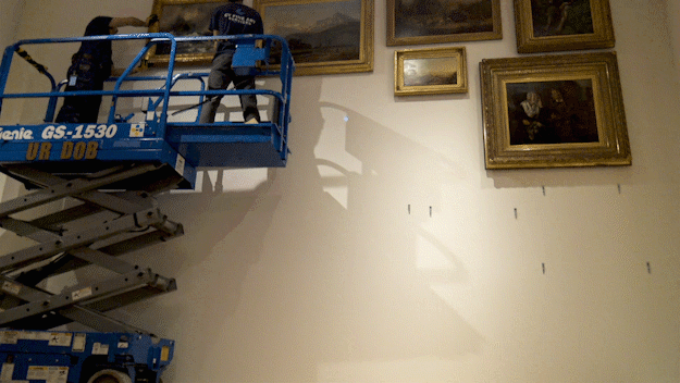 Timelapse gif of artworks being hung on a large wall using a lift.
