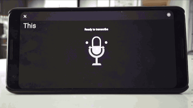 A phone sitting on a table showing live transcribe in action outputting captions as someone offscreen speaks