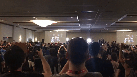 A crowd of hundreds in a conference room suddenly burst into cheer by jumping and raising their hands.