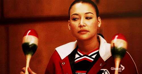 Santana from glee shaking marracas and looking bored
