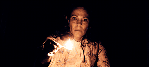 A woman holding a match in the darkness. Two hands come near her head and clap.