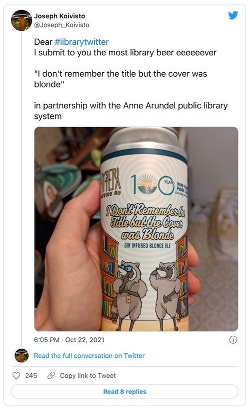 a tweet at the link shown. Image is of a hand holding a can of beer with a cartoon of two biped raccoons standing in front of a bookshelf. name if beer is I Don’t Remember The Title But The Color was Blonde
