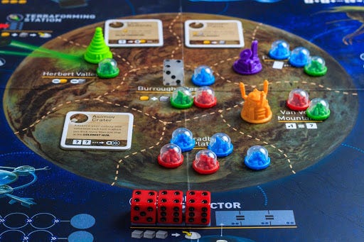 a game board of a planet that has sections to place cards or tokens the tokens are multicolored domes with colonies in them