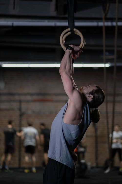 Image of a male gymnast pulling doing a pull up on rings.
