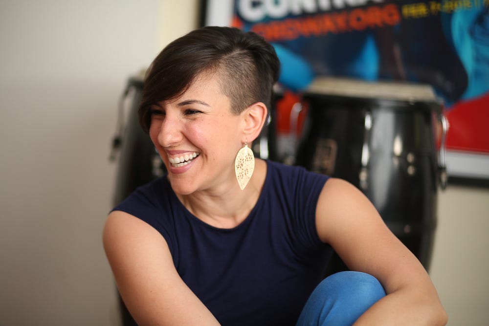 Woman with dark brown hair wears dark blue shirt, white dangling earrings