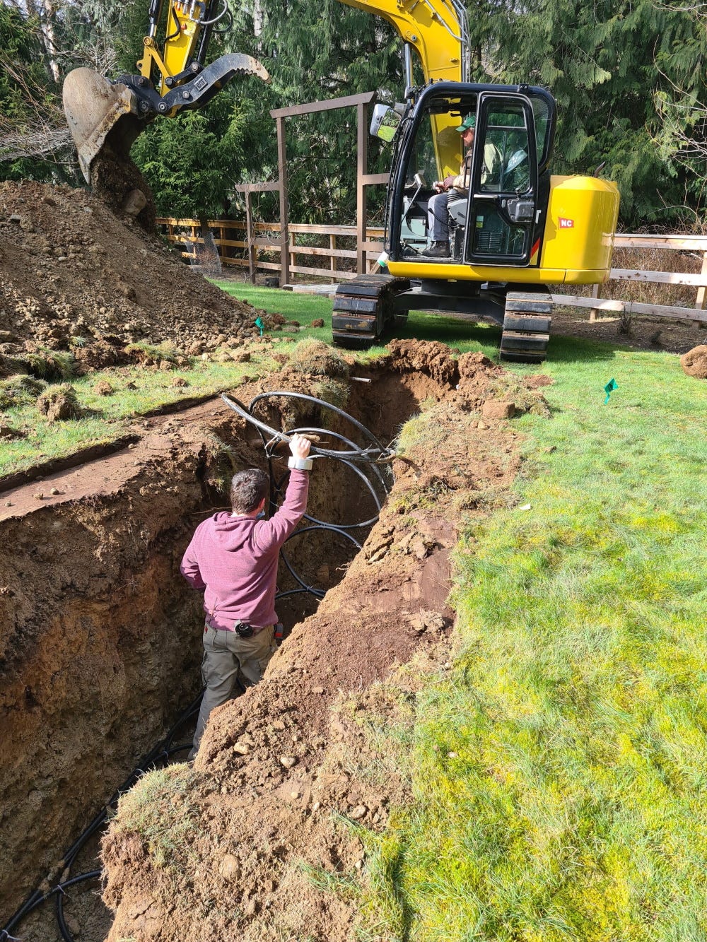 Excavator digging a trench through the yard, installer standing in the trench, shorter than the sides.