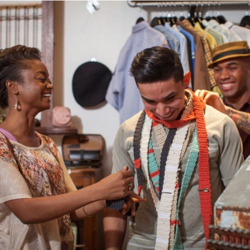 Three people in vintage shop, many trying on crocheted scarves