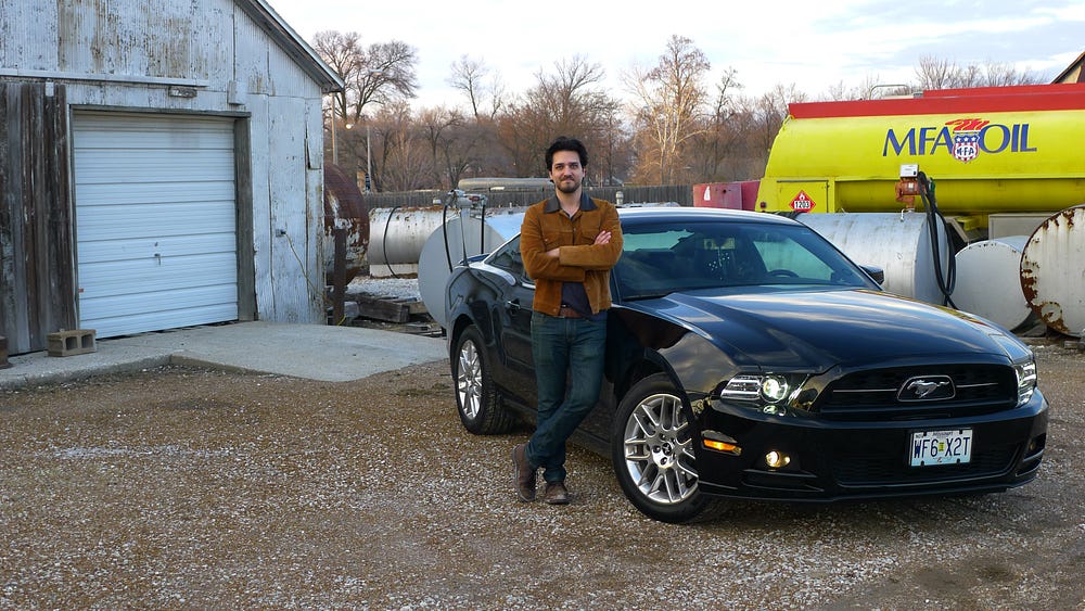 An image of the author standing next to his black 2014 Ford Mustang.