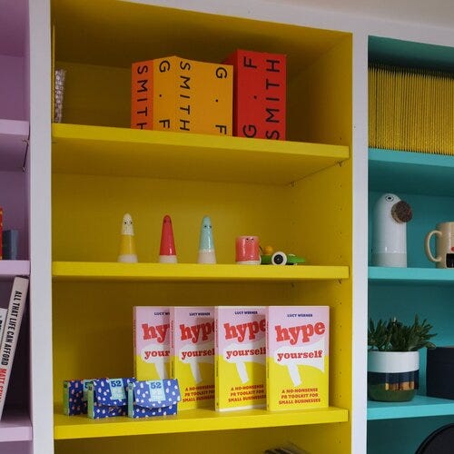 My yellow office shelves with mock-ups of my book Hype Yourself