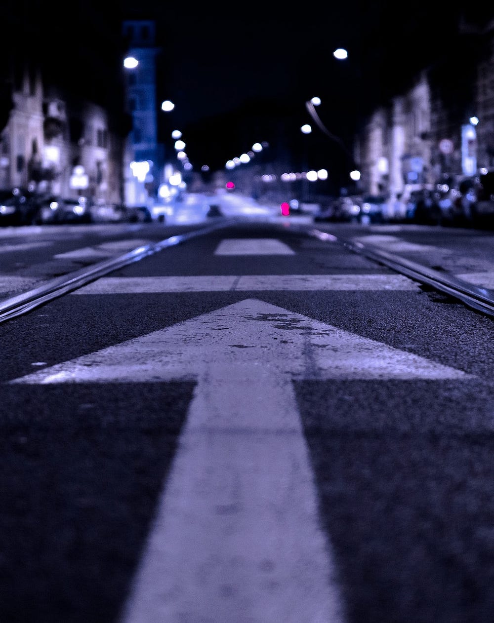 Streetscape at night featuring a city street with an arrow painted on it, pointing straight ahead
