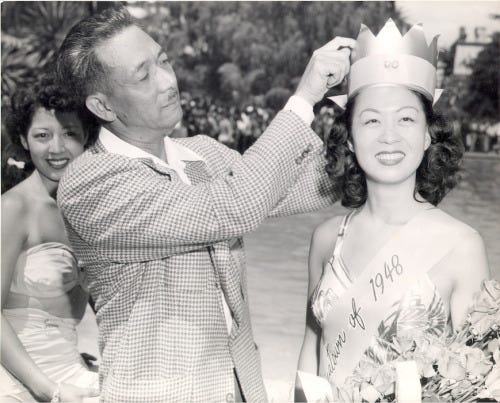 A man places a crown on Penny Lee Wong’s head. Wong is smiling and holding a bouquet of flowers.