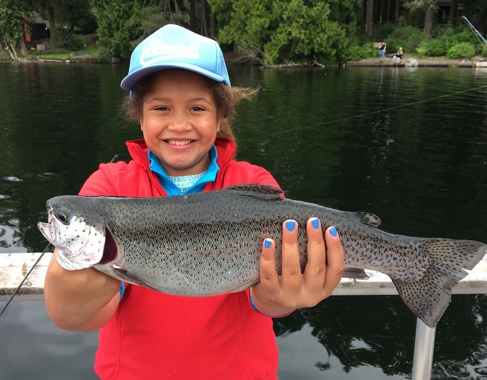 Young girl holding a rainbow trout she just caught in both her hands.