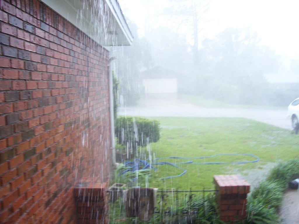 Rain pouring down side of brick house.