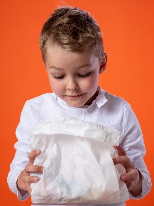 A child is looking inside of a white paper lunch bag.