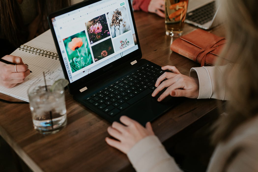 A person operating a laptop on a desk with a cup of ice beside the laptop