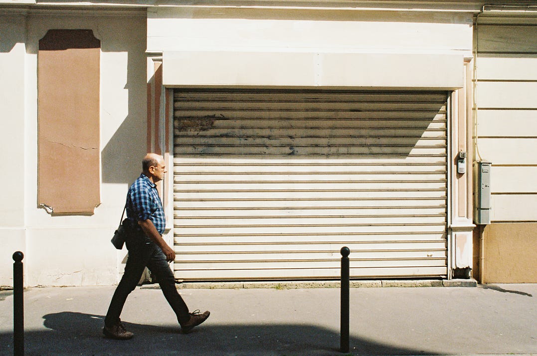 Street Photography; a man walks along a street, a shutter in the background