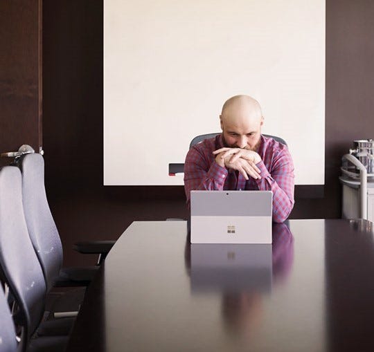 Man in long sleeve shirt, Kris Rivenburgh, closely studies the screen on a Microsoft surface in a conference room.